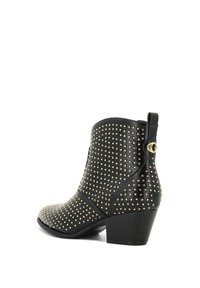 Botines de cuero negro hasta el tobillo con una punta afilada, decorados con tachuelas doradas y una pestaña lateral para tirar. Cuentan con un tacón grueso para mayor estabilidad.