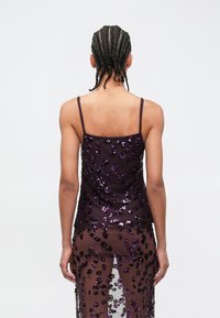 Μωβ διάφανο τοπ με λεπτές τιράντες, διακοσμημένο με παγιέτες σε λουλουδάτο μοτίβο, φορεμένο πάνω από μια διάφανη φούστα που ταιριάζει.