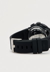 Zwarte digitale sporthorloge met een gestructureerde rubberen band, zilveren gesp en een zichtbare achterzijde die details van de waterbestendigheid toont.