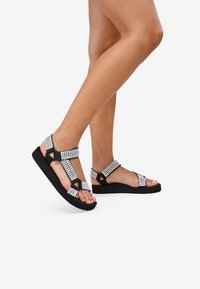 Sandalias negras con correas adornadas con cristales, con suela plana y hebillas ajustables. Las correas texturizadas proporcionan un ajuste seguro.