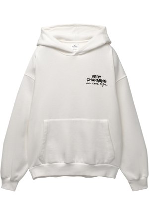 Hoodie blanc en tissu doux, avec une poche avant, de coupe oversized, et texte imprimé en noir : "TRÈS CHARME EN VRAI".