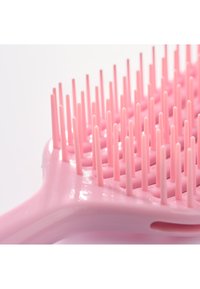 Close-up van een roze haarborstel met flexibele kunststof haren die gelijkmatig verdeeld zijn over een geventileerde basis.