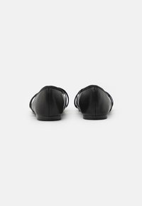Zapatos planos negros con un acabado suave similar al cuero, punta redondeada y delicadas correas entrecruzadas en los lados, con un tacón bajo y sólido.