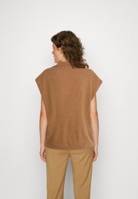 Top castanho de malha com gola, mangas em forma de copo e um corte solto, combinado com calças bejes. Textura suave, calor subtil.