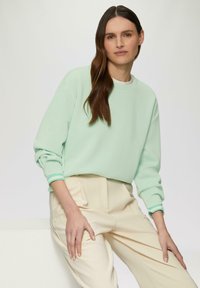Mintgroene sweatshirt met ronde halslijn en opgerolde mouwen, gedragen met crèmekleurige broek met plooien en een ontspannen pasvorm.