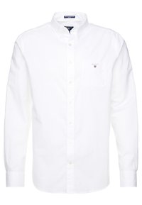 Chemise blanche à manches longues avec col boutonné, une poche poitrine simple, et un logo discret de la marque brodé sur la poche. Tissu en coton lisse.