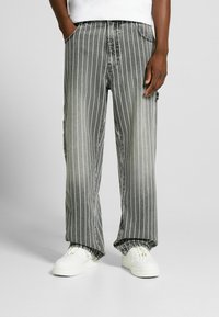 Jeans di denim a righe in nero e grigio con vestibilità morbida, dotati di strisce verticali bianche e tasche. Abbinati a sneaker bianche.