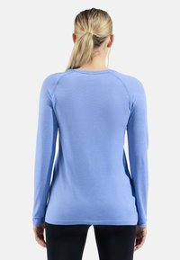 Haut à manches longues bleu clair avec un tissu texturé, décolleté rond et manches raglan, présentant un ourlet légèrement cintré et une silhouette ajustée.