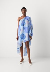 Axelklänning i ljusblå chiffon med blå blommönster, asymmetrisk fåll och flödande silhuett. Bärs med vita klackskor.