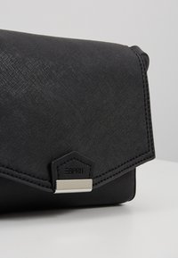 Pochette Esprit noire texturée avec rabat et fermoir rectangulaire argenté sur une surface claire.