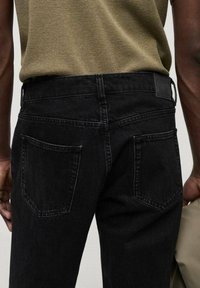 Vaqueros de denim negro con corte recto, cinco bolsillos y una etiqueta de cuero cerca de la cintura. La textura está ligeramente desgastada.