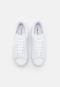 Hvite skinnsneakers med rund tå, flate skolisser og lys rosa merke. Har en teksturert såle og en polstret innersåle for komfort.