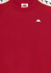 Felpa rossa Kappa con logo bianco sul petto e strisce sulle spalle che presentano figure logo nere e bianche ripetute.