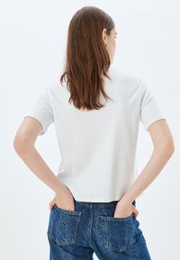 Camiseta blanca de manga corta de algodón, con cuello redondo, corte relajado y textura suave; combinada con jeans de mezclilla azules.