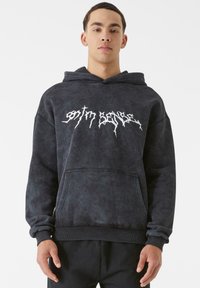 Juodas, per didelis gobtuvas, pagamintas iš minkštos, tekstūruotos medžiagos. Yra priekinė kišenė ir balti grafikos užrašai ant krūtinės. R ribuoti rankovių ir apatiniai kraštai.