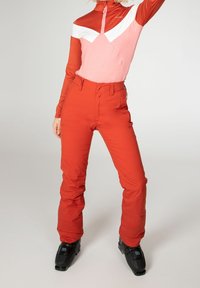 Pantalons de ski rouges à taille haute et coupe ajustée, associés à un haut à manches longues en bloc de couleurs avec des sections roses, rouges et blanches.
