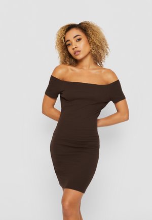 Smeđa haljina bez naramenica, seđena od mekanog materijala, s bodycon siluetom koja ističe figuru, dužine do sredine butina.