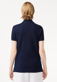 Polo shirt bleu marine à manches courtes et col classique ; texture lisse, détails de couture subtils ; coupe ajustée.