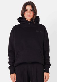 Zwart oversized hoodie met een zak aan de voorkant, verstelbare capuchon en logodetail. Gemaakt van zachte stof met geribbelde manchetten en zoom.