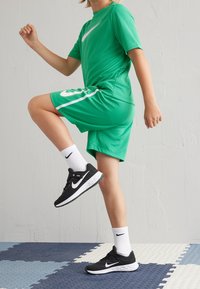 Grünes Nike Sportoutfit bestehend aus einem T-Shirt mit kurzen Ärmeln und Shorts, mit einem weißen Logo, kombiniert mit schwarzen Nike Sneakers und weißen Socken.