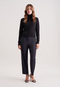 Czarny golf w połączeniu z dopasowanymi ciemnymi spodniami, charakteryzującymi się gładką teksturą i eleganckim fasonem, dopełniony czarnymi sandałami na obcasie.