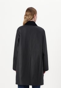 Casaco longo preto com um colarinho alto, fenda nas costas e corte reto. Feito de um material suave e leve, adequado para sobreposições.