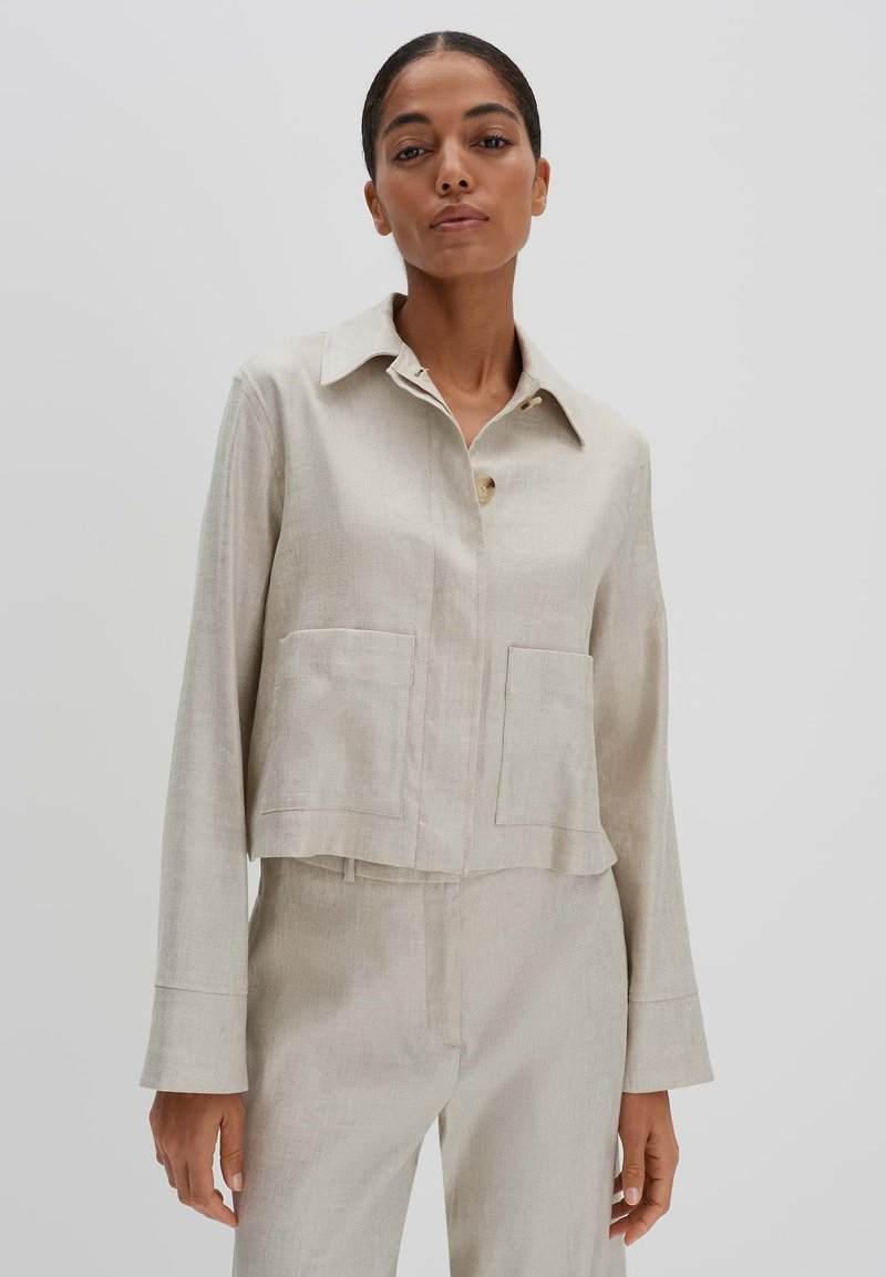 Lichtbeige cropped jack gemaakt van textuurstof, met een knoopsluiting aan de voorkant, een spitse kraag en twee grote zakken aan de voorkant.