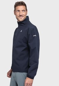 Marineblauer wasserdichter Parka mit hohem Kragen, langen Ärmeln und elastischen Bündchen. Verfügt über ein kleines Logo auf der linken Schulter und einen Frontreißverschluss.