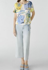 T-shirt a maniche corte, multicolore, con motivi astratti, abbinato a jeans a gamba larga blu chiaro e sandali con plateau blu.