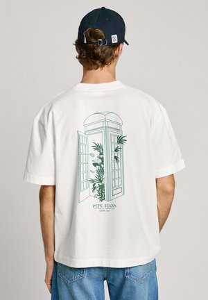 T-shirt en coton blanc avec un dessin de ligne vert d'une cabine téléphonique à sonnette ouverte avec des plantes à l'arrière. Manches courtes et coupe décontractée.
