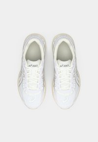 Weiße Sportschuhe aus Mesh und Leder, mit runder Form und strukturierten Laufsohlen. Besitzt Schnürsenkel und ein Logo auf der Zunge.