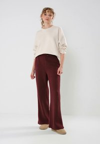 Lys beige strikket genser med rund hals og oppbrettede ermer, kombinert med burgunder bukser med vidde som har en strukturert overflate og elastisk midje.