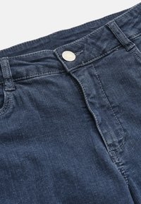 Tummansininen farkkukangas, jossa on napin suljenta, erottuva ompelu ja sileä pinta. Näkyvä vyötärö ja vetoketju.