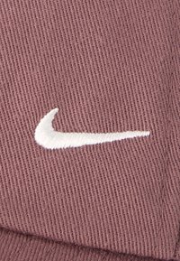 Κοντινό πλάνο καφέ υφάσματος με λευκό κεντημένο λογότυπο Nike swoosh.