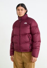 Bordeauxfärgad pufferjacka med hög krage, dragkedjestängning och två sidofickor. Har quiltade sektioner och en liten logga på bröstet.