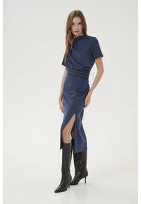 Navy blue satin midi dress with short sleeves, side ruching, and a thigh-high slit, paired with knee-high black heeled boots.