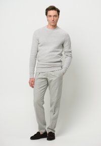 Lichtgrijze gebreide trui met ribbels aan de mouwen, gecombineerd met lichtgrijze broek. De outfit wordt aangevuld met donkergroene suède instappers.