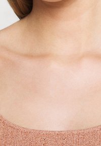 Różowo-złoty top z miękkiej, teksturowanej tkaniny, z zaokrąglonym dekoltem i delikatnym prążkowaniem na krawędziach, prezentujący gładkie wykończenie.