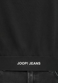 Čierne bavlnené tričko s textúrovaným pásom a bielym brandingom "JOOP! JEANS". Tričko má jednoduchý, klasický dizajn.