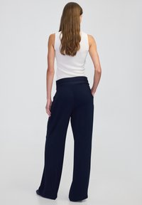 Granatowe spodnie szerokie w nogawkach z wysokim stanem i tylnymi kieszeniami. W połączeniu z dopasowanym białym topem bez rękawów. Gładka tekstura, casualowy design.