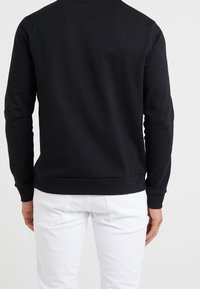 Schwarzer Baumwollpullover mit langen Ärmeln und rundem Kragen. Mit einem gerippten Saum und Bündchen versehen. Rückansicht dargestellt.