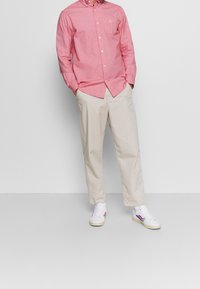 Rode blouse met knopen en een zak, gecombineerd met beige broek en witte sneakers met rode en blauwe accenten. Glad stoffen textuur.