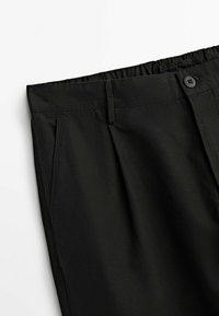 Pantalons noirs en tissu texturé, dotés d'une taille élastique, fermeture à bouton et poches latérales. Conçus pour le confort et la flexibilité.