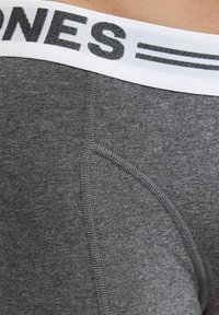 Grauetrikot-Stoff Boxershorts mit einem weißen Bund, der mit schwarzem Markierungstext versehen ist. Sichtbare Nähte entlang der Nähte für Langlebigkeit.