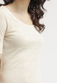 Beżowa koszulka w paski z okrągłym dekoltem, krótkimi rękawami, miękką fakturą i dopasowanym krojem.