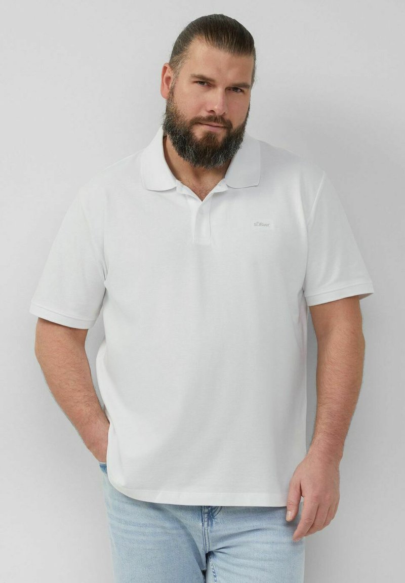 Weißes Polo-Shirt aus Baumwolle mit klassischem Kragen, kurzen Ärmeln und einem dezenten Logo auf der Brust. Kombiniert mit hellblauen Jeans.