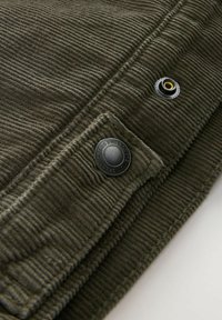 Tela de pana verde oliva con nervios verticales, que presenta un botón de presión negro y un ojal de metal, mostrando un detalle texturizado.