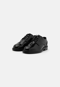 Scarpe stringate in pelle nera con finitura lucida, punta tondeggiante, dettagli di cucitura discreti e tacco basso e robusto.