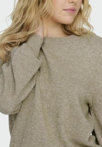 Ljusbeige stickad tröja med rund hals, ribbade ärmslut och subtilt strukturerat mönster. Mjuk material med lös passform, lämplig för att lagra.