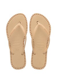 Des tongs beiges avec semelle en caoutchouc, semelle intérieure texturée et bords tissés. Fines brides avec détail de la marque. Taille 37-38 indiquée.